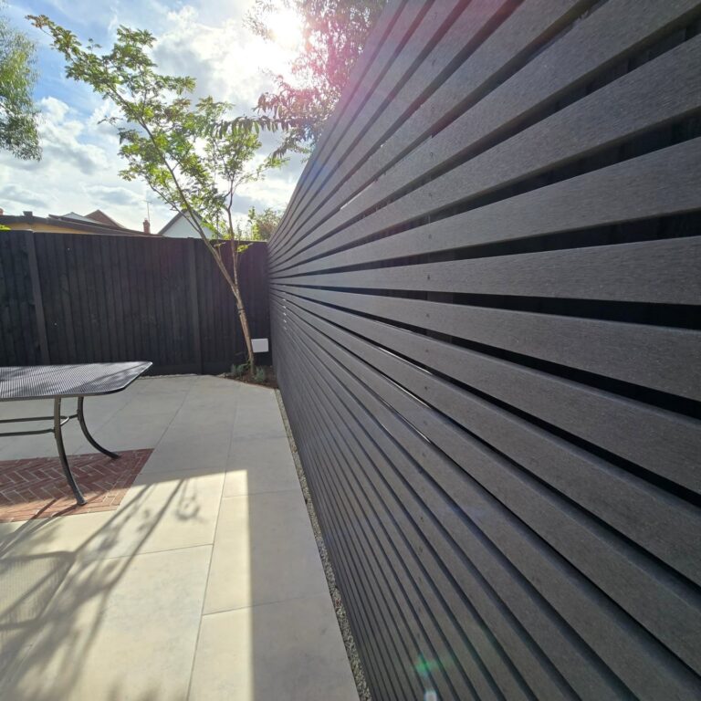 Perspective view of a slatted modern fence panel with porcelain patio and small tree